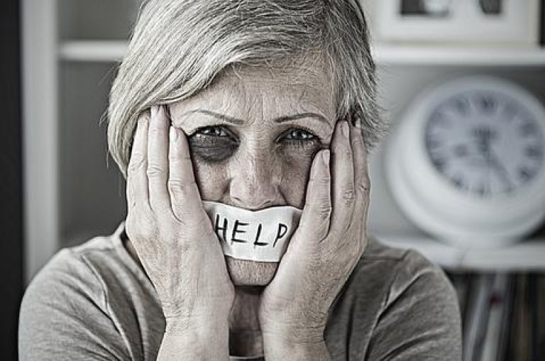 Elderly woman with bruised eye with tape in mouth with HELP written on it